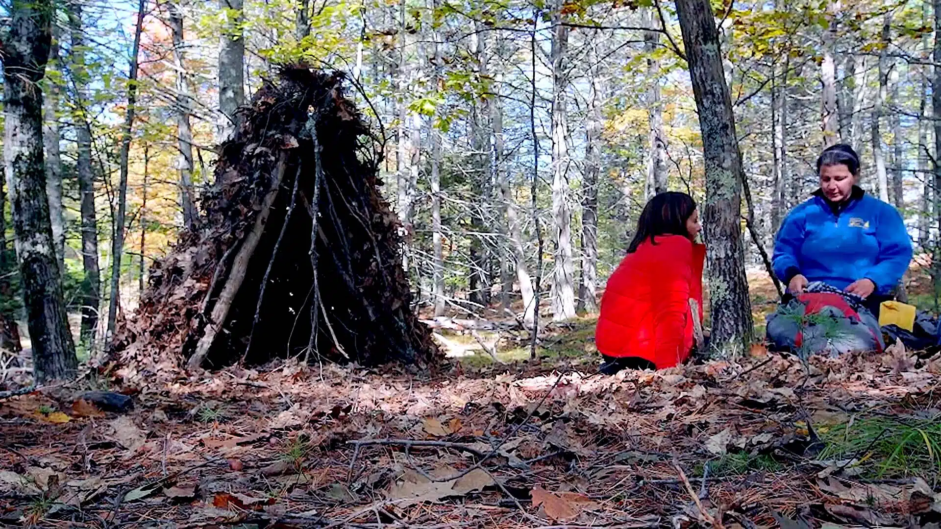 two people sitting in the woods next to a hut.