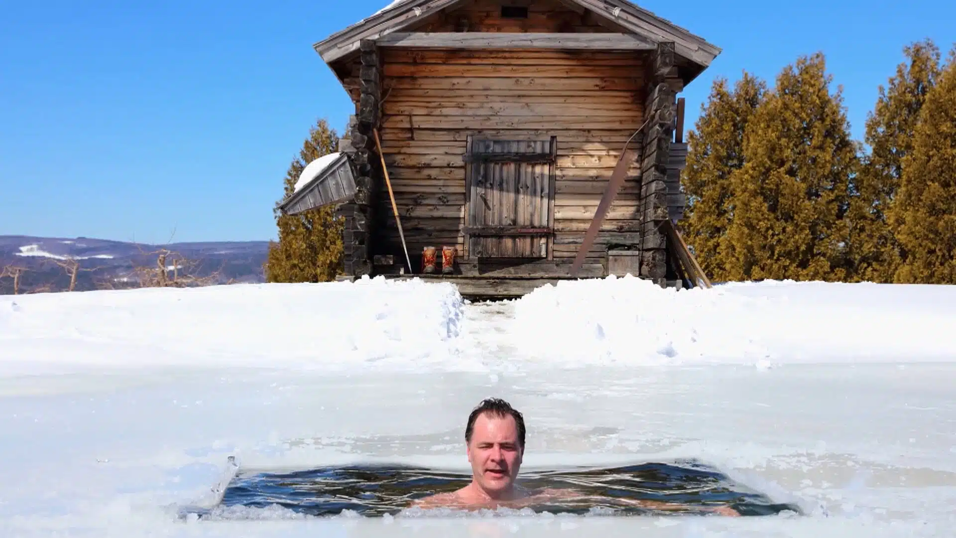Eric Aho in a frozen lake in front of a wooden building.