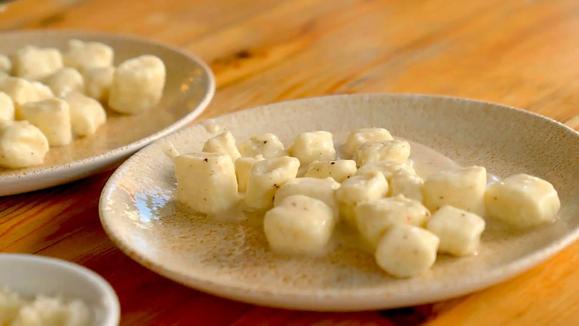 Two plates of gnocchi in a creamy sauce are placed on a wooden table.