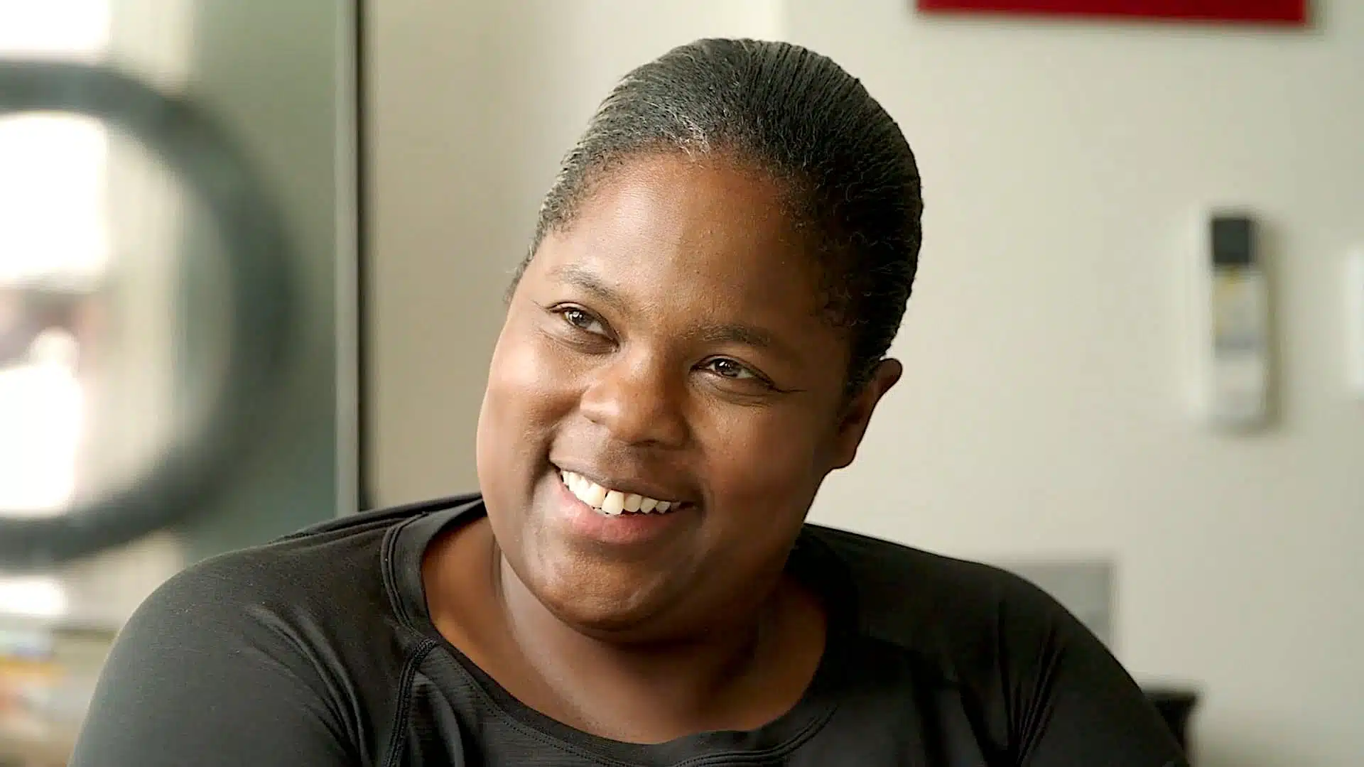 A person with a friendly smile, wearing a black top, is looking slightly to the right.