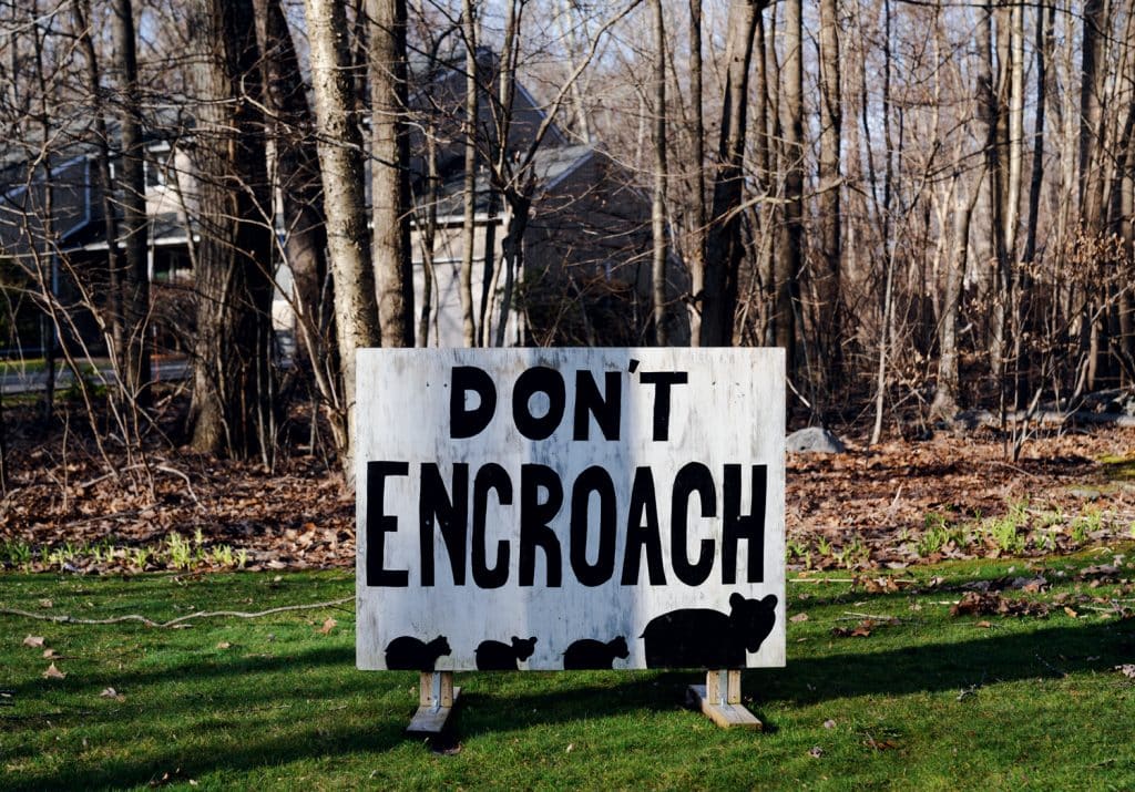 A sign in front of a forested area reads "DON'T ENCROACH," with images of rodents silhouette at the bottom.