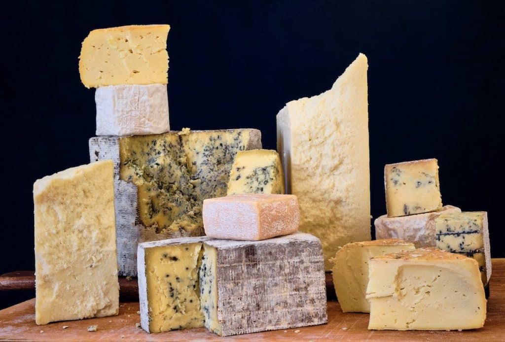 A variety of cheeses arranged on a wooden surface against a dark background.