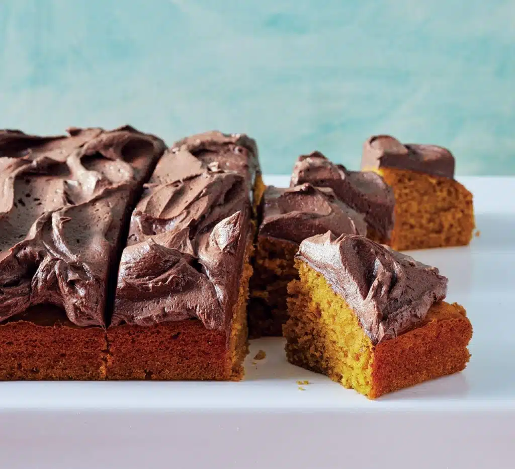 A frosted rectangular cake pumpkin with chocolate icing, with some pieces cut and slightly separated, displayed on a white surface.