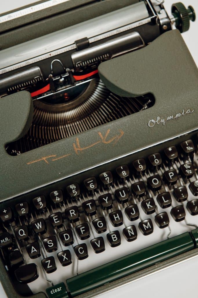 Close-up of a green Olympia typewriter with visible keyboard and typebars. Some writing and a symbol are engraved above the keys.