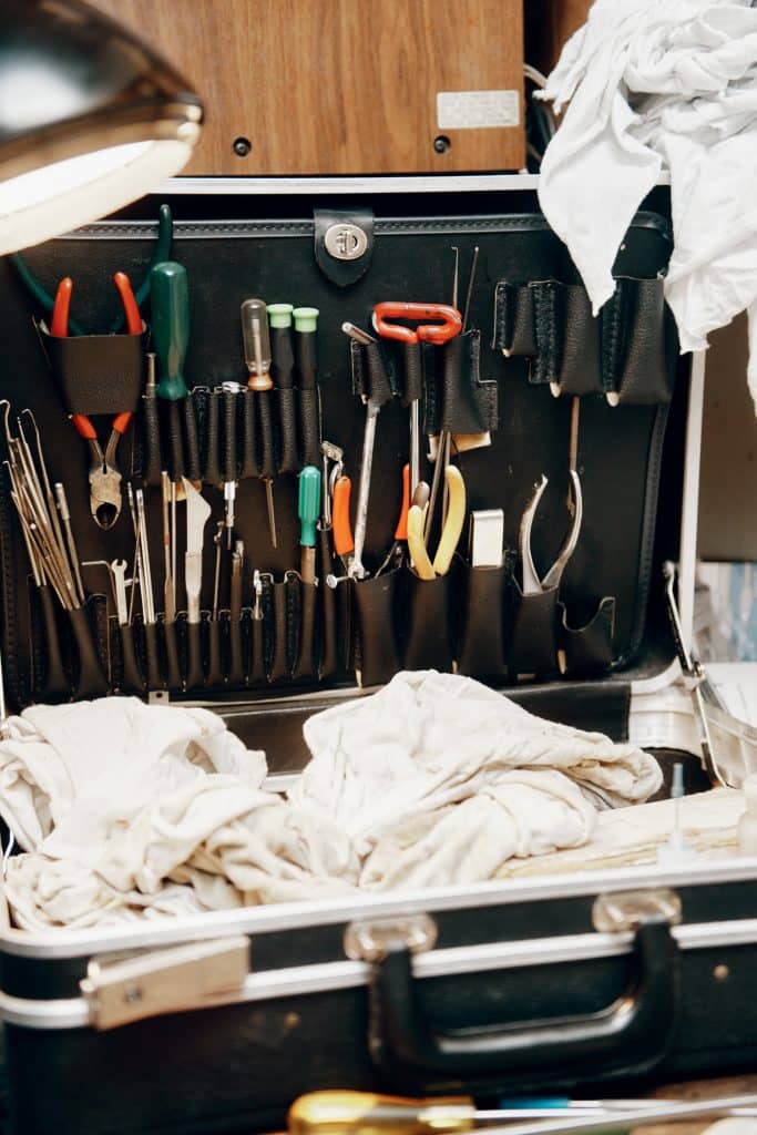 An open toolkit with various tools, including pliers, screwdrivers, and wrenches neatly organized. White cloths are placed nearby.