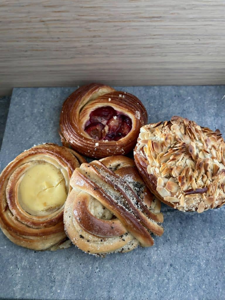 A selection of four pastries are displayed on a gray surface. They include a fruit danish, an almond-topped pastry, and two other pastries with cream fillings.