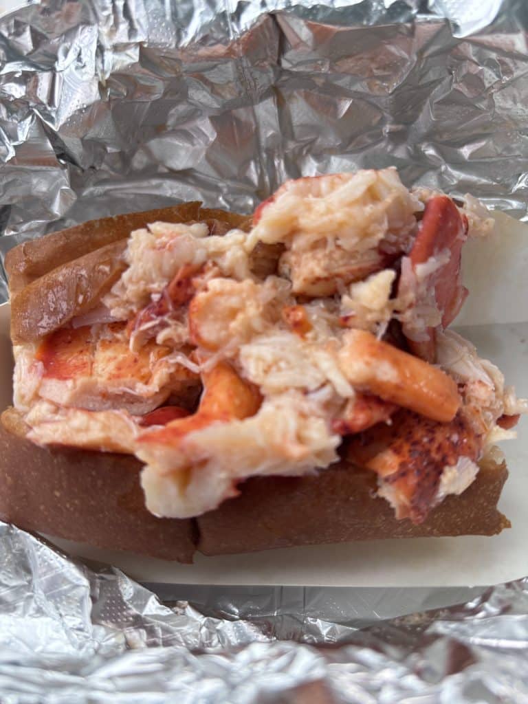 A lobster roll with chunks of lobster meat in a bread roll, wrapped in foil.