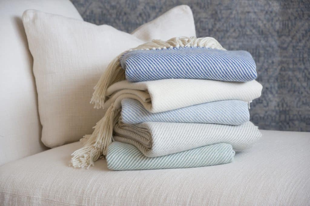 A stack of folded blankets in blue and neutral tones is placed on a cream-colored sofa.