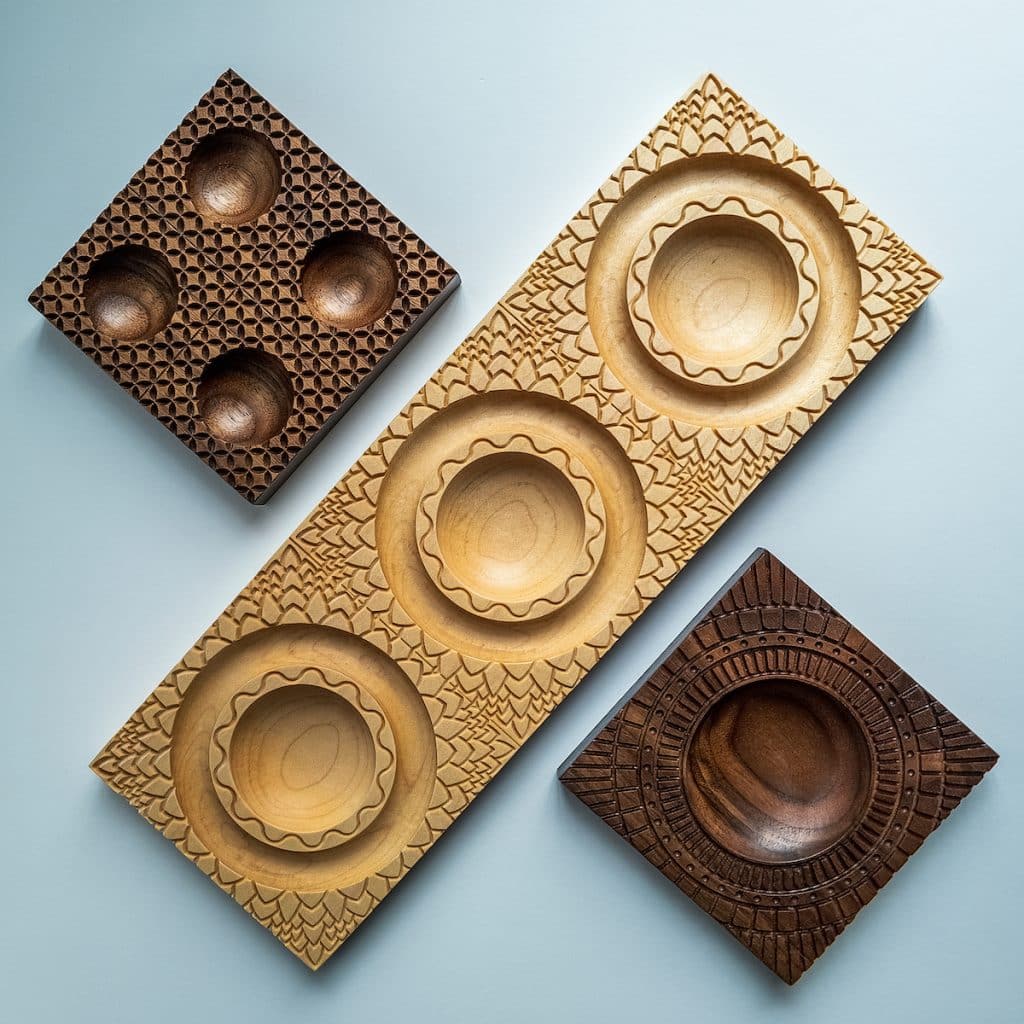 Three intricately carved wooden trays with circular indentations, arranged on a light blue surface.