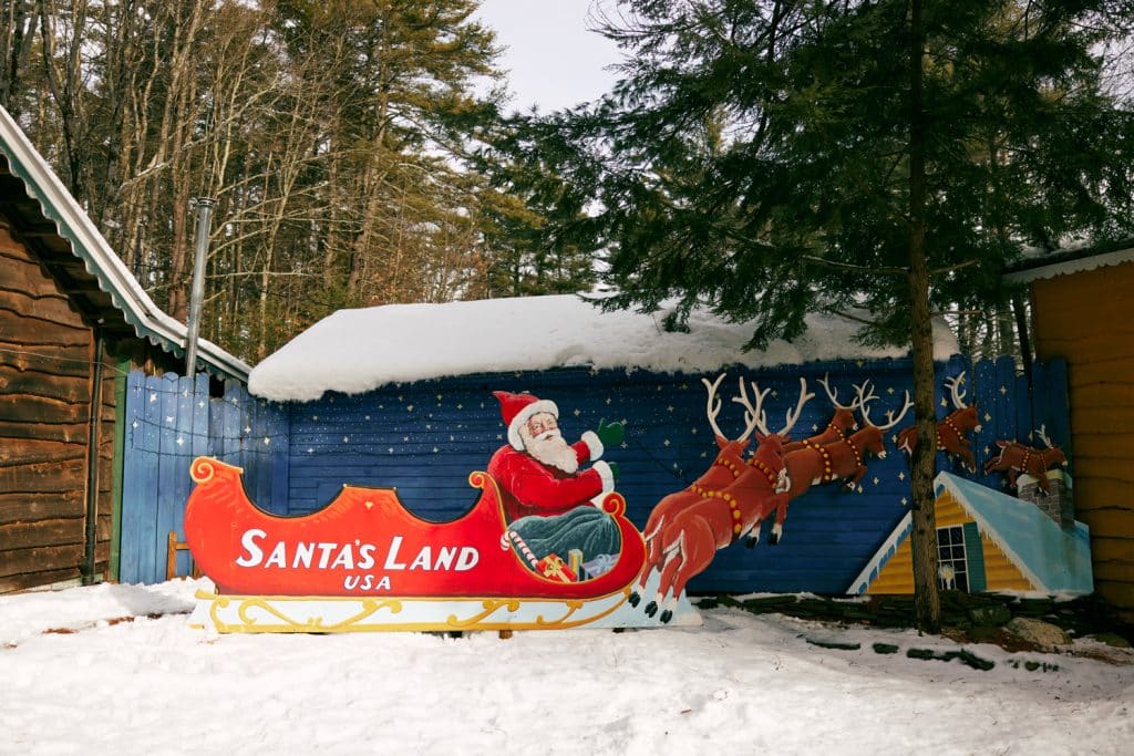 A mural at Santa's Land USA features Santa Claus in a sleigh pulled by reindeer, set in a snowy scene under trees.