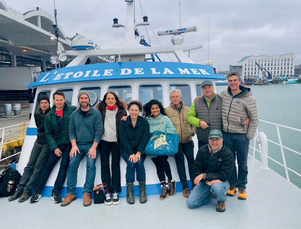 A group of people posing on a boat named "L'Etoile de la Mer" at a harbor.