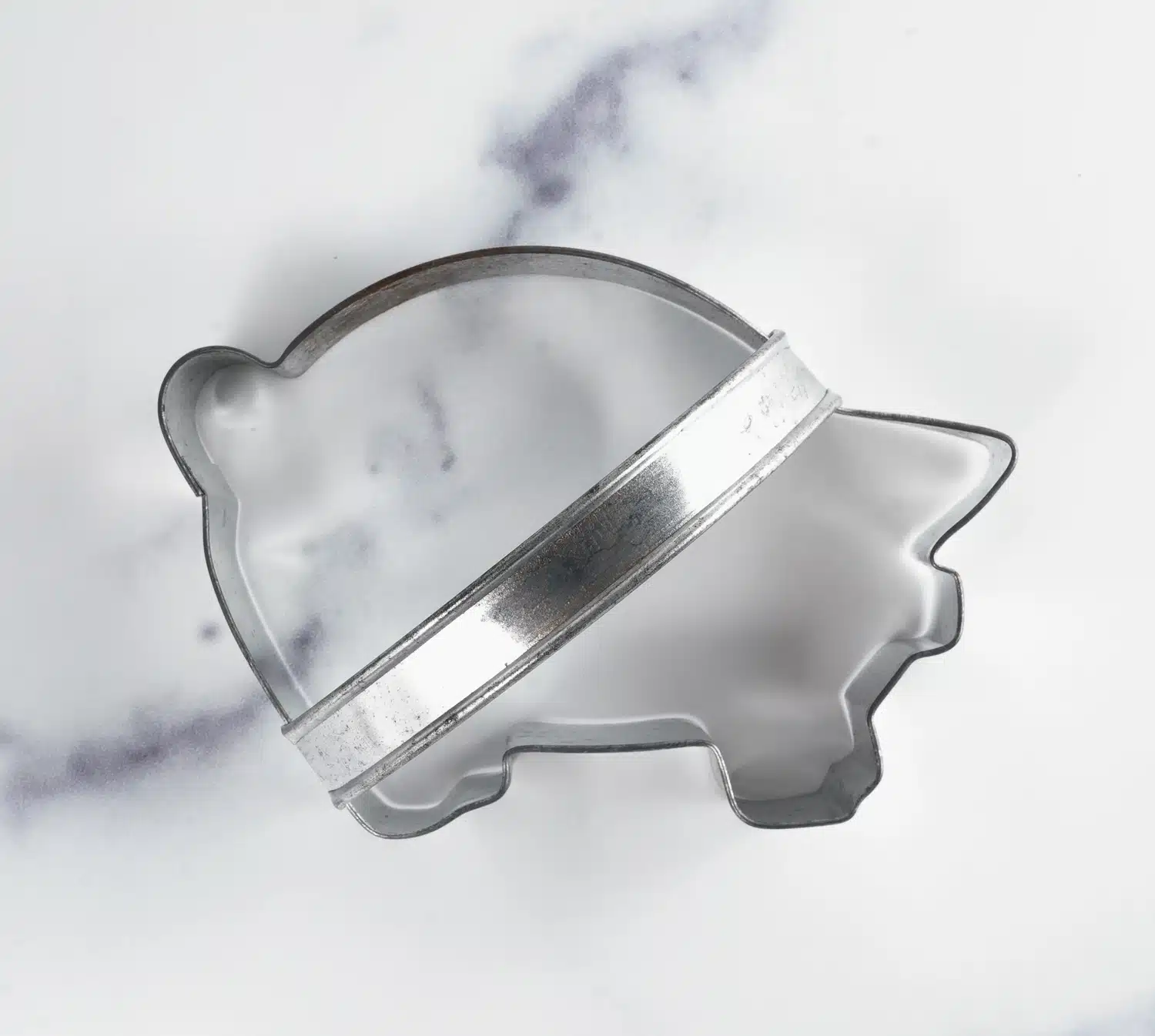 Metal cookie cutter shaped like a hippo, placed on a white marble surface with gray veining.