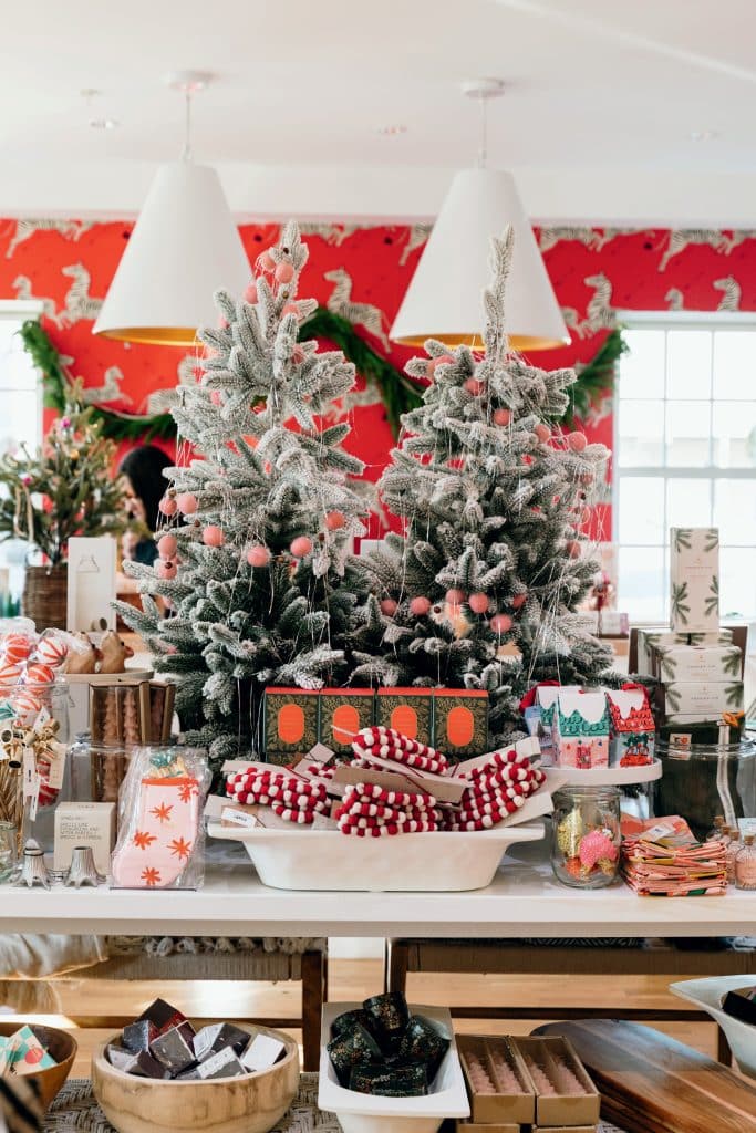 A festive store display with small decorated Christmas trees, wrapped gifts, and various holiday-themed products on a table.