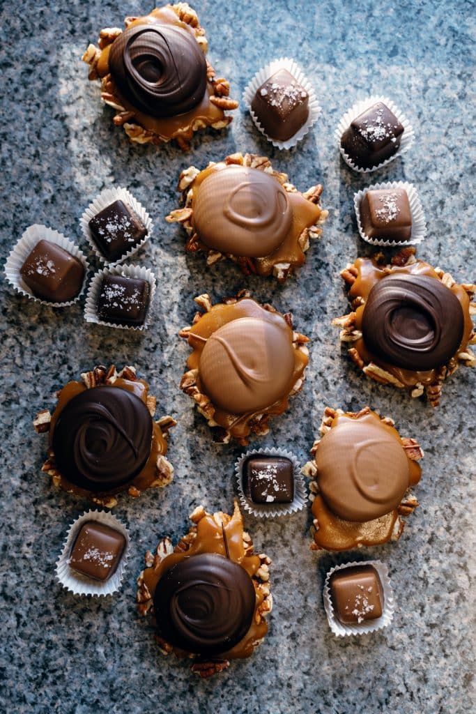 Assorted chocolate-covered caramel clusters and boxed chocolates arranged on a granite countertop.