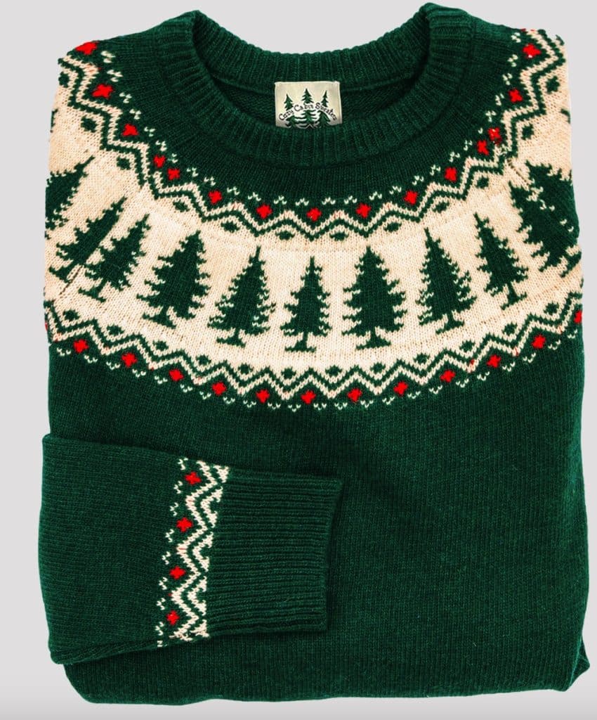 A folded green sweater with a white and red Nordic pattern featuring tree silhouettes around the chest and wrist.