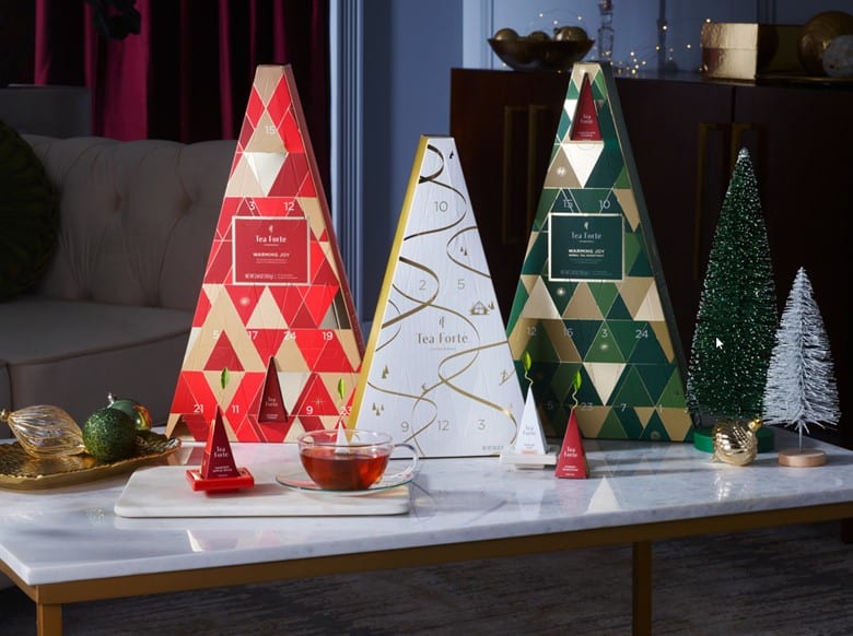 Advent calendars shaped like trees and a cup of tea on a table, with decorative trees in the background.