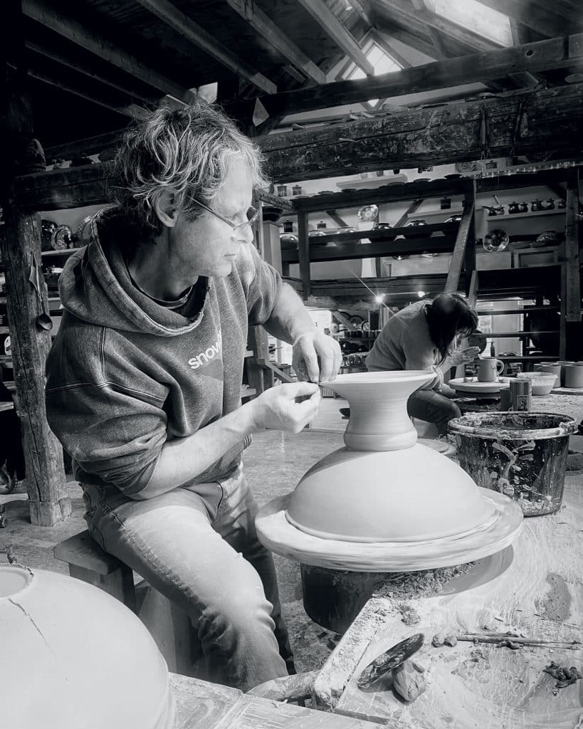 Two people crafting pottery on wheels in a workshop, focusing intently on shaping clay.