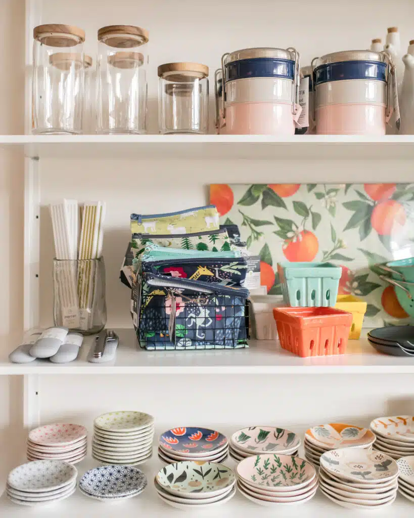 Shelves with jars, stacked tiffins, napkins, colorful berry baskets, and patterned plates neatly arranged.