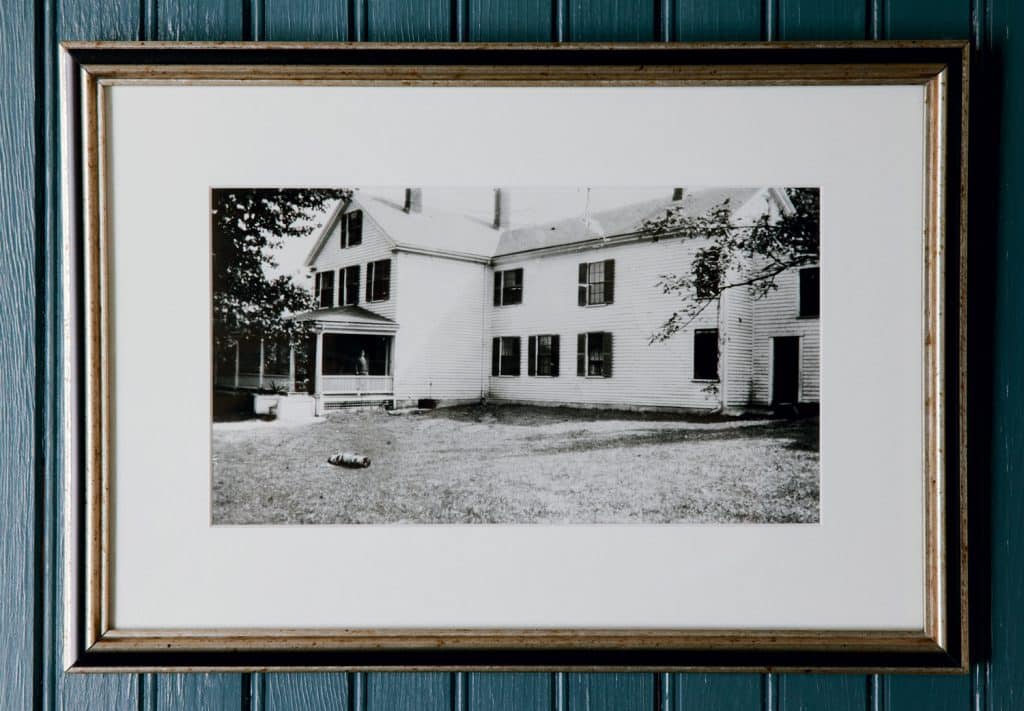 Framed black and white photograph of a large, two-story house with several windows and a porch, displayed on a teal-paneled wall.