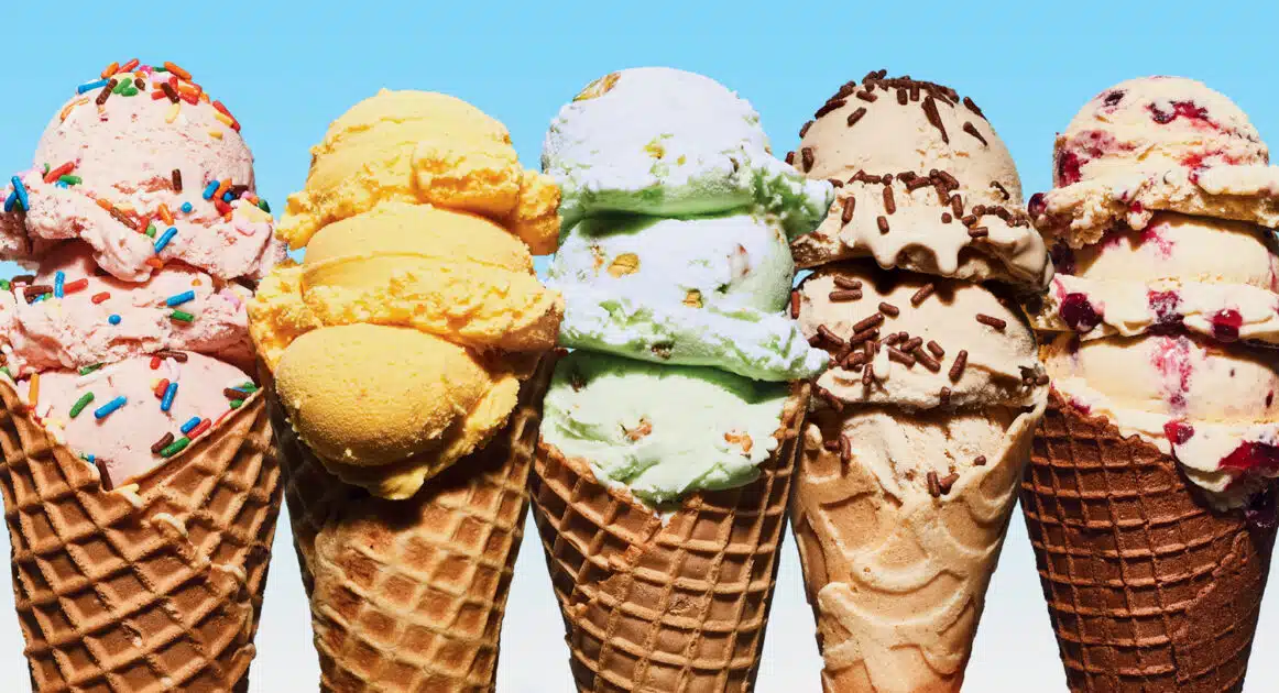 Five ice cream cones with different flavors and toppings are lined up against a blue background.