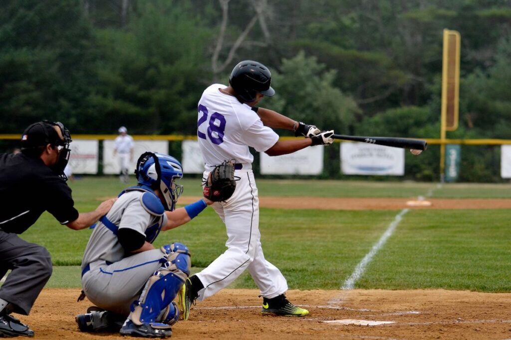 A baseball player in a white uniform hits a pitched ball while the catcher and umpire observe behind home plate.