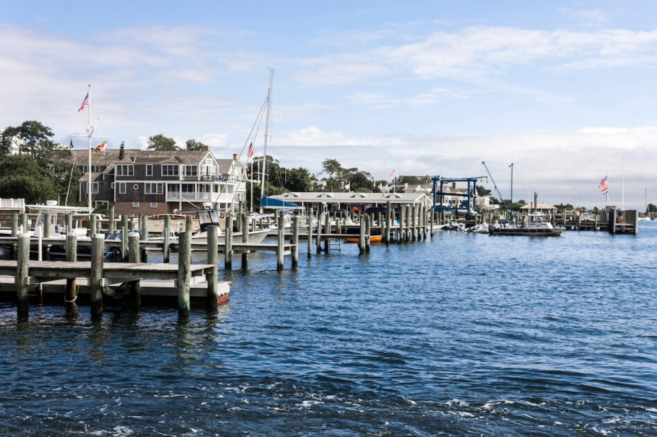 A marina with wooden docks, boats, and waterfront buildings under a partly cloudy sky.