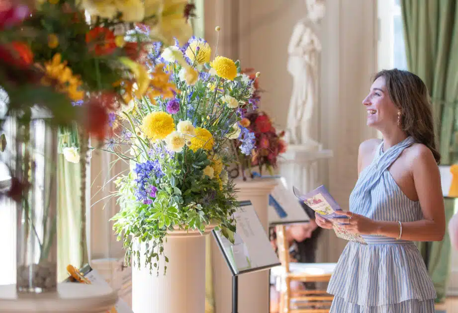 Woman in a striped dress smiles at colorful flower arrangements during the annual Newport Flower Show.