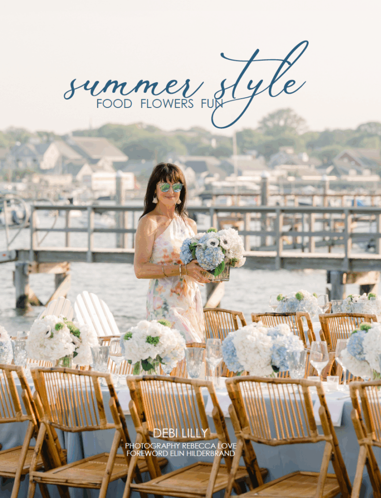 A woman in a floral dress stands by a long outdoor table set with blue and white flowers by the water, with docked boats and houses in the background. Text overlay reads "summer style."