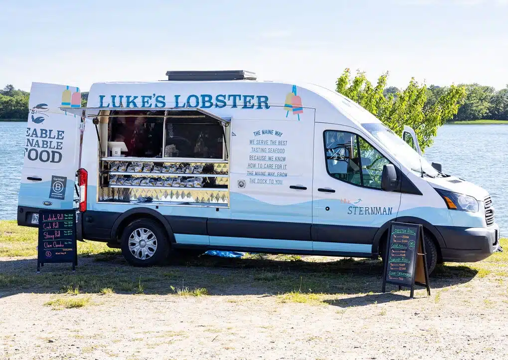 A Luke’s Lobster food truck parked by the water with menu boards displayed outside.