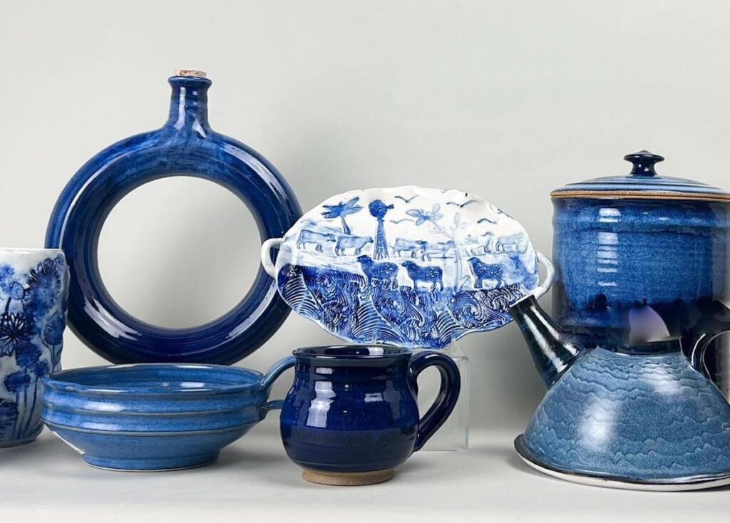 A collection of blue and white ceramic and porcelain items, including mugs, plates, a teapot, a circular vase, and a patterned dish, arranged against a neutral background.