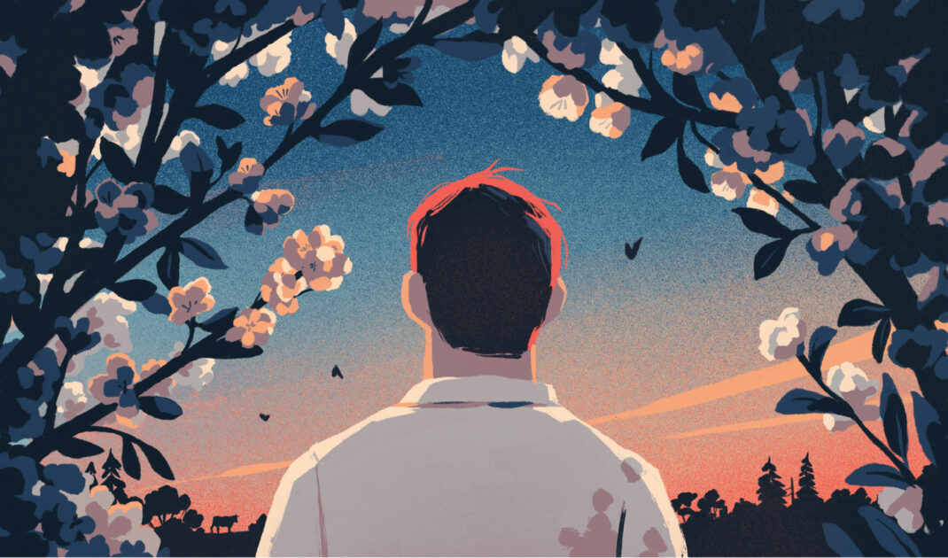 A person with short red hair stands facing a sunset, framed by flowering branches and silhouetted trees in the background.