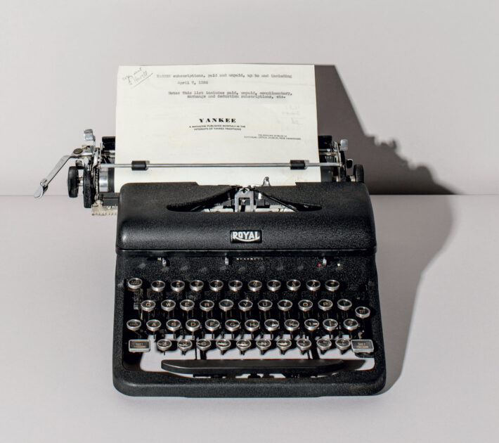 A black Royal typewriter with a typed sheet of paper inserted, set on a plain surface against a neutral background.