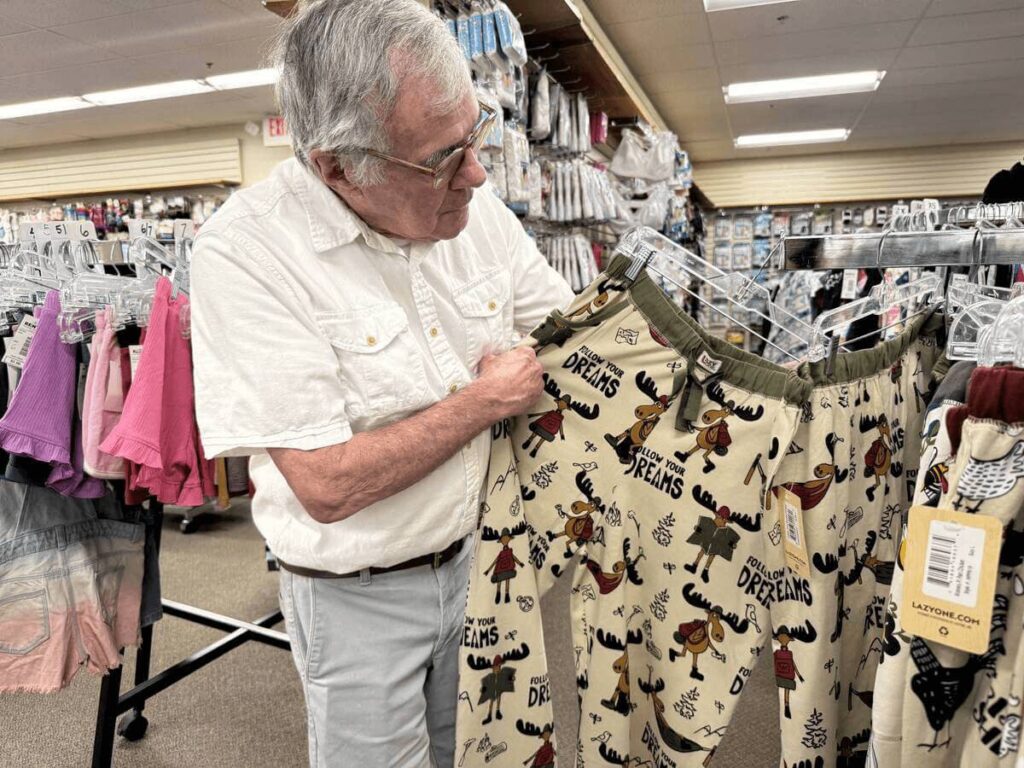 Man holds up pajama pants decorated with moose and the word Dreams at Renys in Maine.