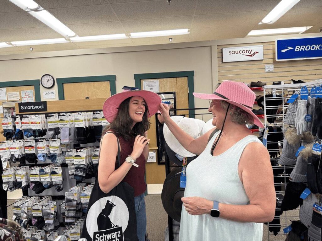 Two women in pink hats laugh together while shopping at Renys in Maine.