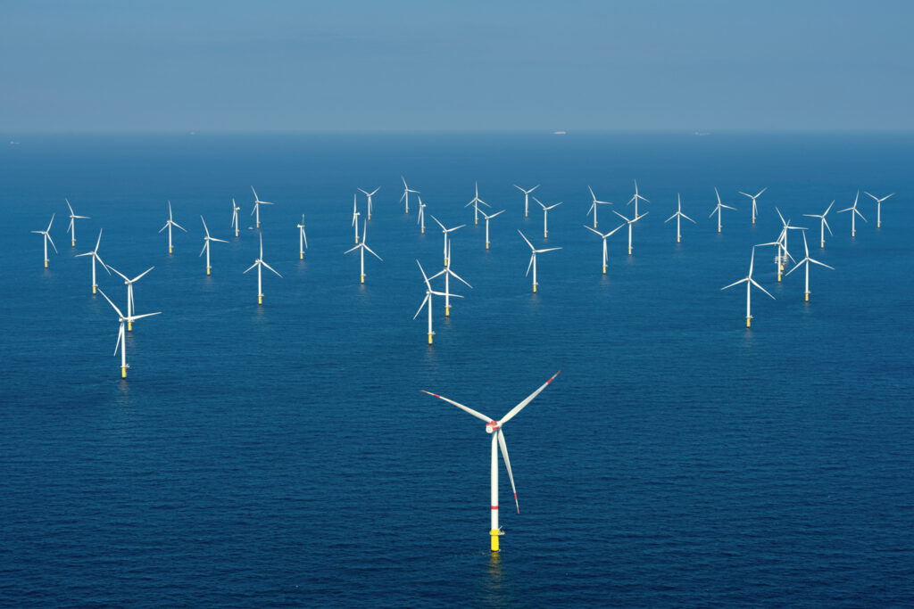 Offshore wind farm with multiple wind turbines standing in the ocean under a clear blue sky.