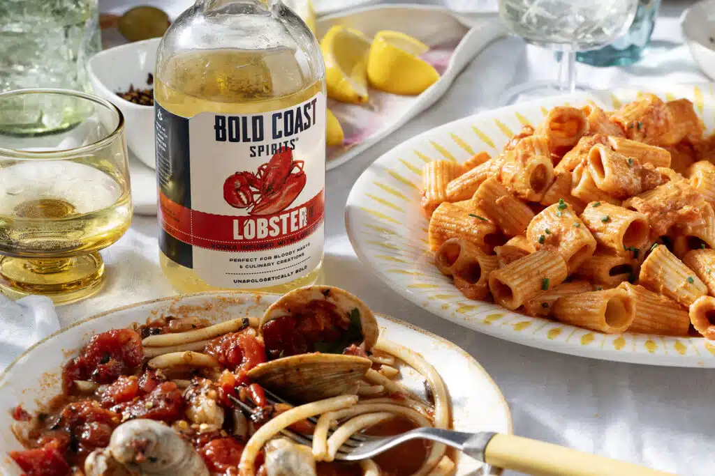 Bottle of Bold Coast Spirits Lobster vodka next to a plate of pasta and seafood.