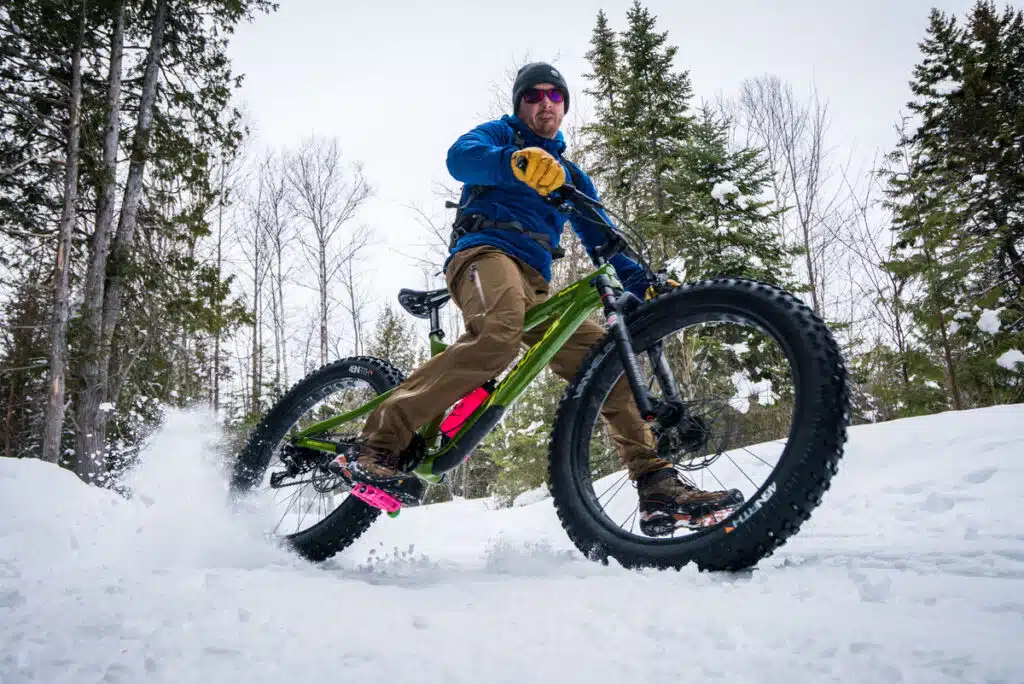 A cyclist riding a fat-tire bike through the snow in a forest.