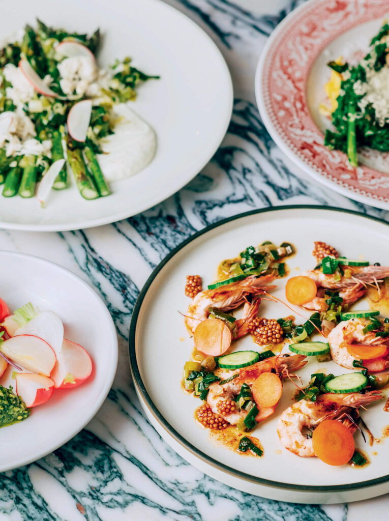 Colorful plates of gourmet salads and shrimp dishes on a marble table, garnished with vegetables and herbs.