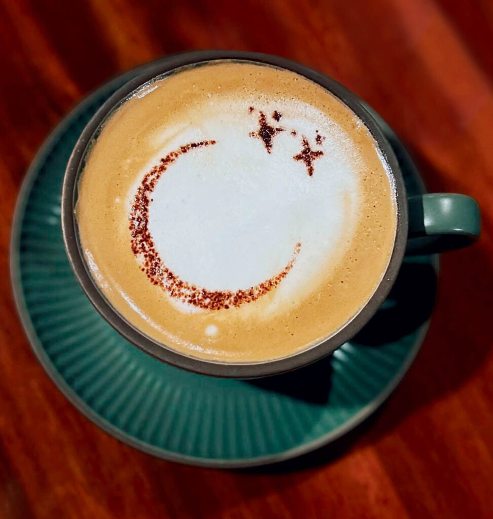 Latte art of a crescent moon and two stars on frothy coffee in a green cup and saucer.