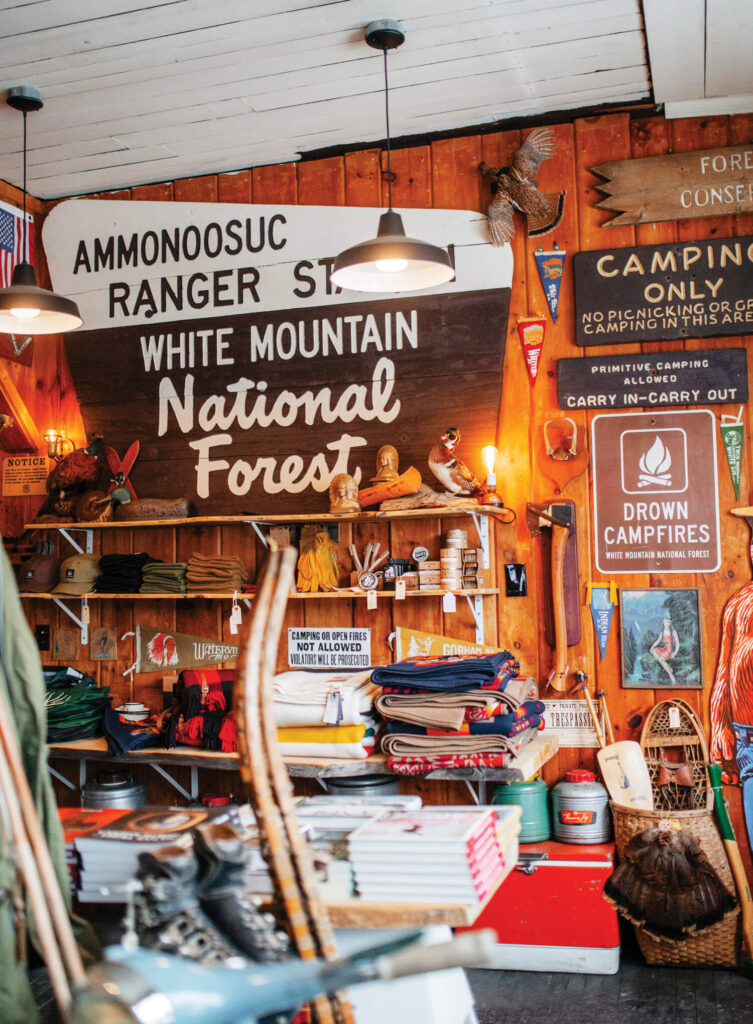 Colorful rustic shop with blankets, signs, books, and camping gear displayed on wooden shelves and walls.
