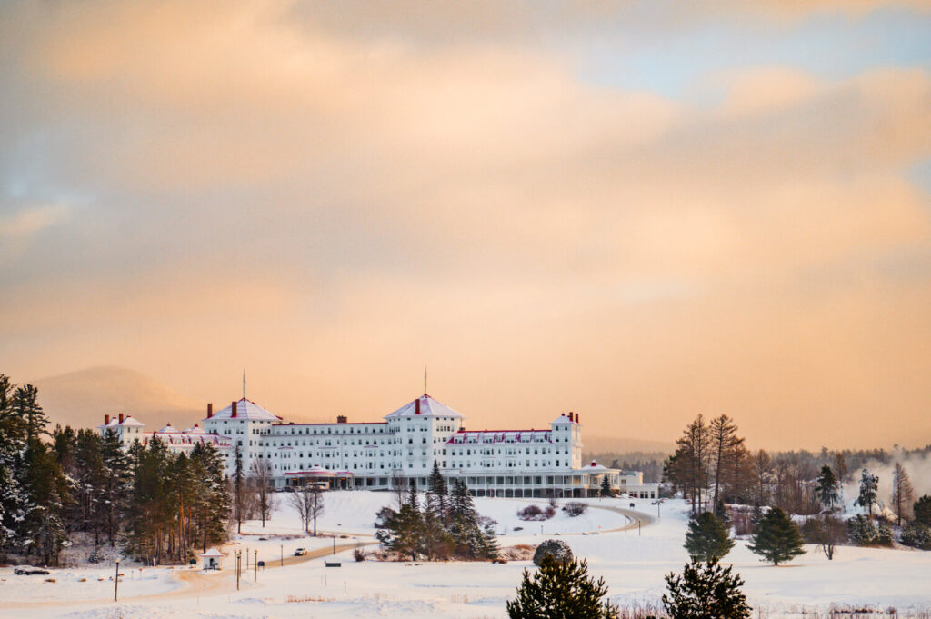 Large white hotel surrounded by snow and trees under a soft, pastel-colored winter sky at sunset. One of many things to do in the White Mountains 