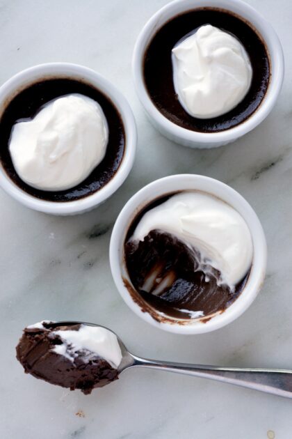 Three ramekins of chocolate pudding topped with whipped cream; one has a spoonful taken out and on the spoon.