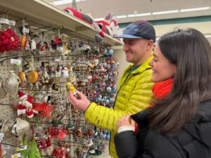 A newlywed couple shops for Christmas ornaments in a Renys store aisle filled with holiday decorations.