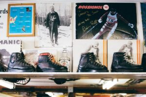 Vintage ski boots on a shelf with old ski photos and memorabilia displayed on the wall behind them.