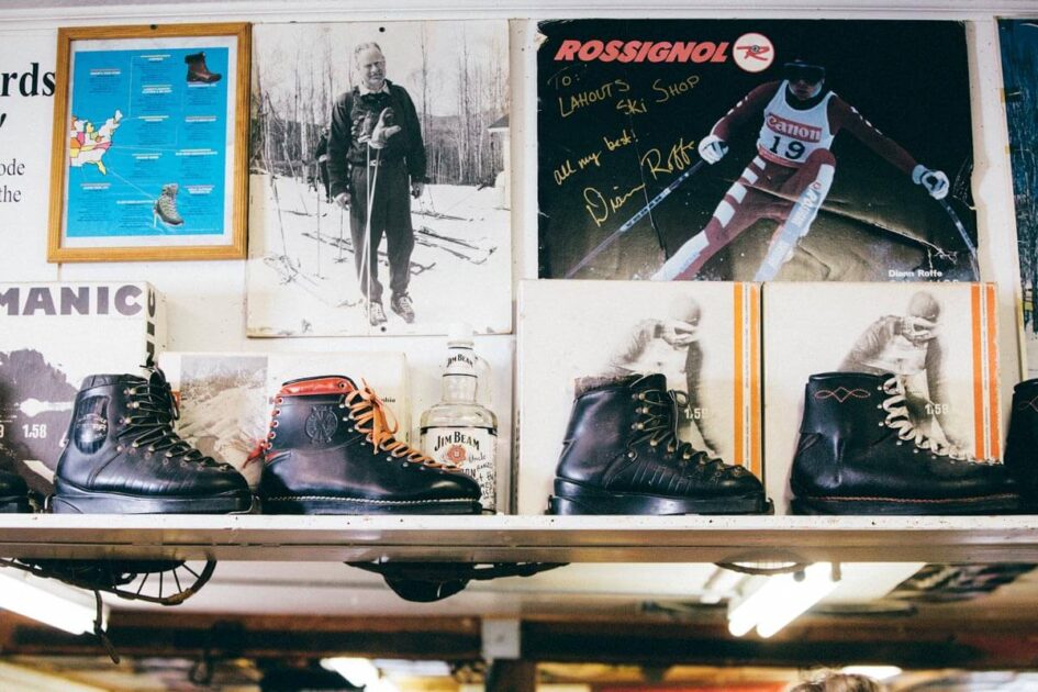 Vintage ski boots on a shelf with old ski photos and memorabilia displayed on the wall behind them.