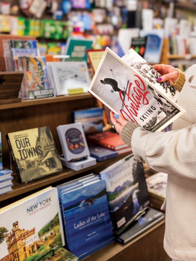 Person holding a book titled "Parallel Skiing" in front of a display of various books in a store.