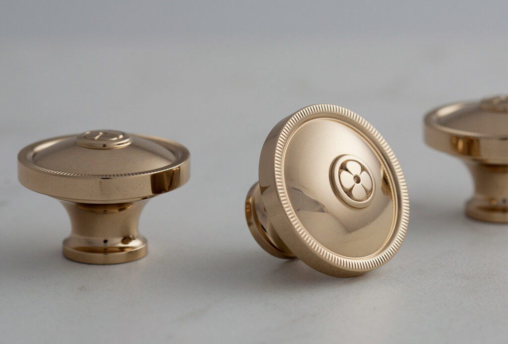 Three shiny gold cabinet knobs displayed on a light surface with a simple, elegant design.