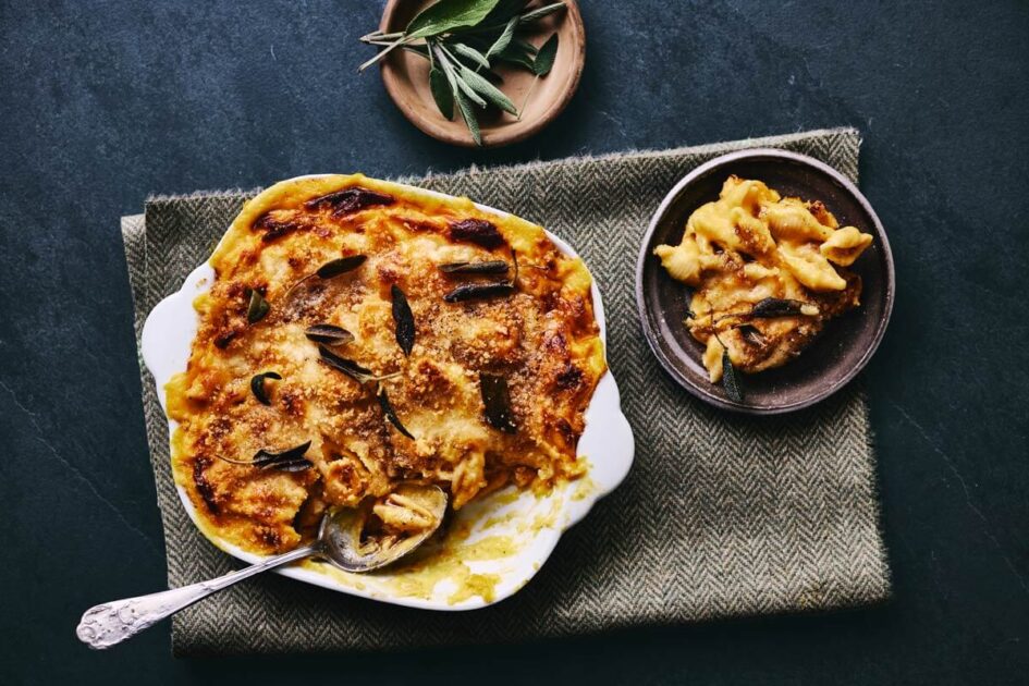 Baked pasta with golden cheese and herbs in a white dish, with a serving on a brown plate nearby.