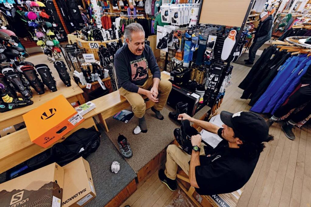 A man tries on ski boots with help from a store employee in a sports gear shop.