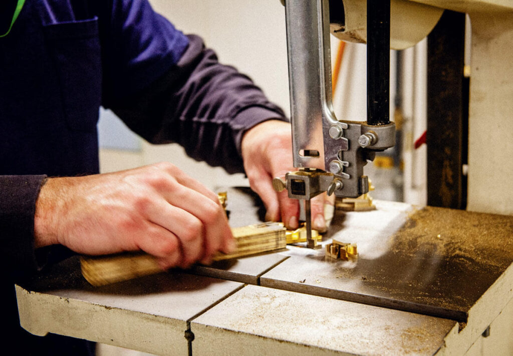 A person uses a bandsaw to cut a piece of wood in a workshop.
